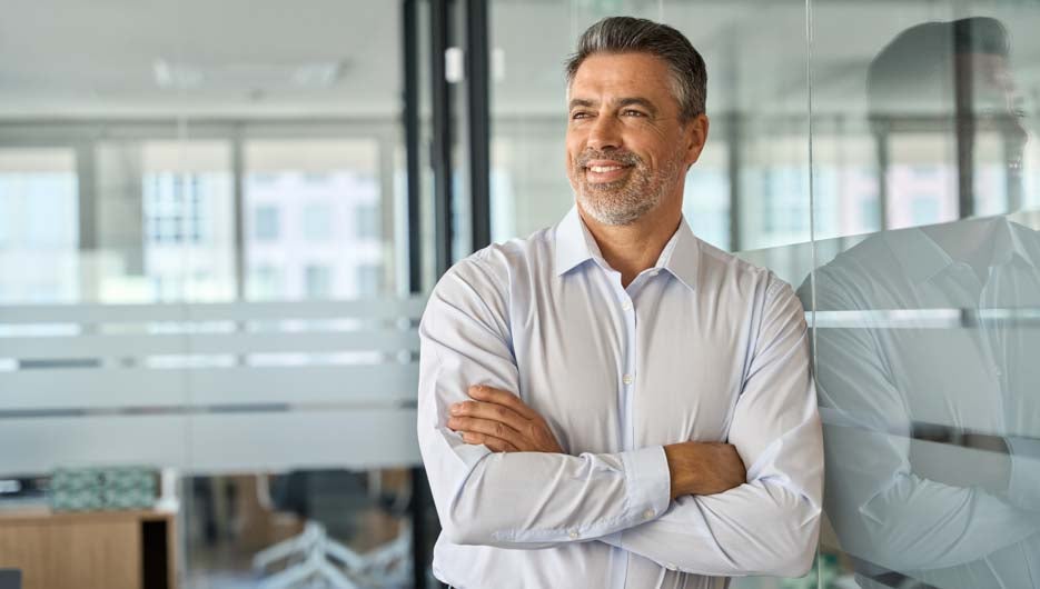 Happy mature latin business man standing in office arms crossed 