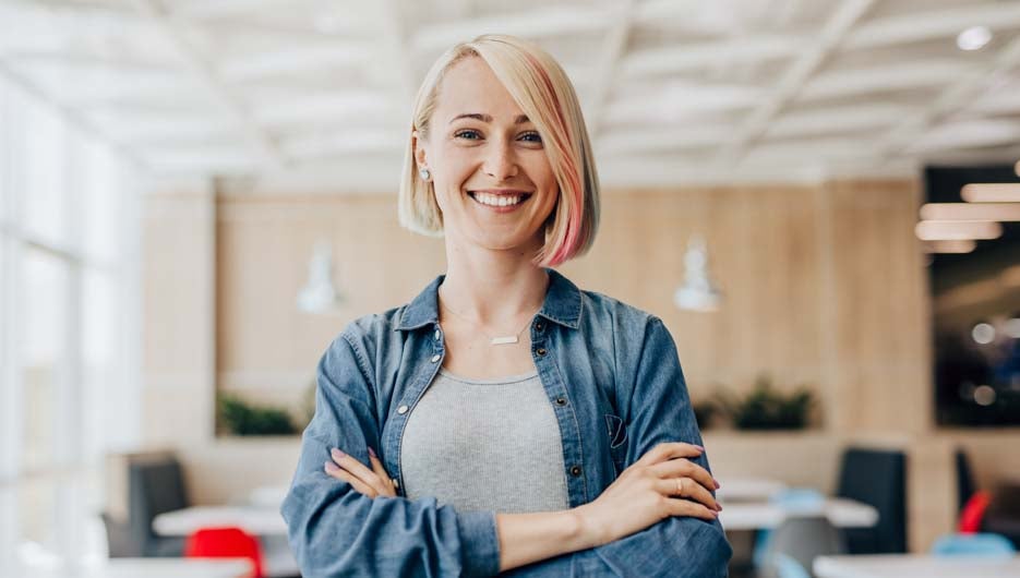 Happy optimistic young female in jeans shirt over grey t shirt standing in cafe and looking at camera